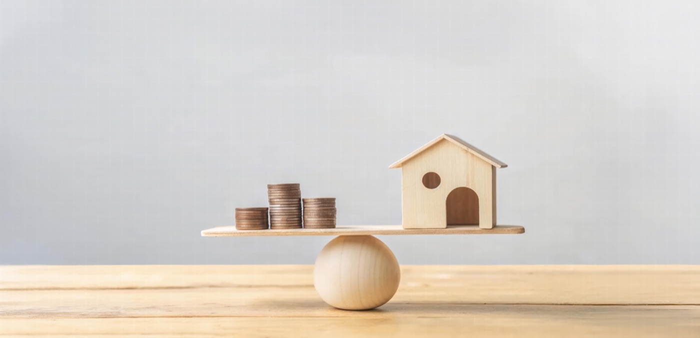 A wooden model house balanced against a stack of coins
